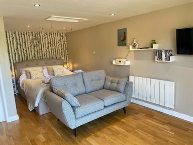 A bedroom with a bed and sofa and a wall-mounted television at Pheasant Lodge in Wimborne Minster
