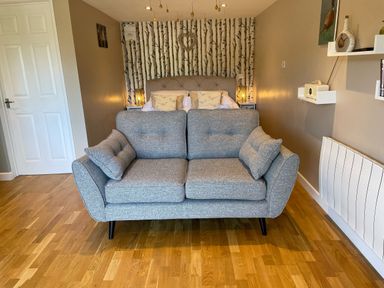 A grey sofa in front of a bed with pillows and bedside tables with lamps in a room at Pheasant Lodge in Wimborne Minster