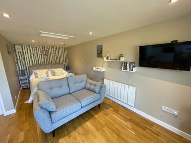A bedroom with a bed sofa television wall shelves and wooden floor at Pheasant Lodge in Wimborne Minster