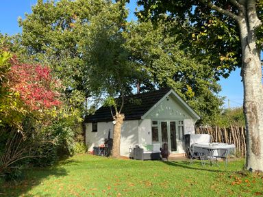 A small house with a garden seating area and trees at Pheasant Lodge in Wimborne Minster