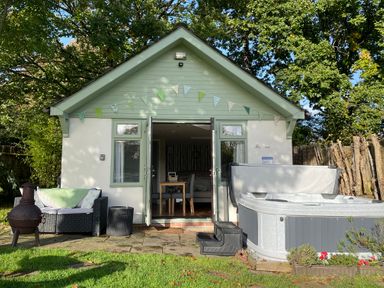 A small house with open double doors a hot tub and a sofa in the garden at Pheasant Lodge in Wimborne Minster