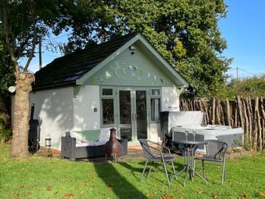 A small building with outdoor furniture a hot tub and bunting in a garden at Pheasant Lodge in Wimborne Minster
