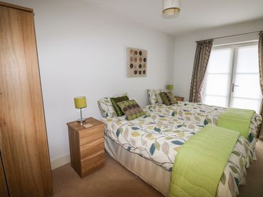 A bedroom with two single beds bedside tables with lamps a wardrobe and a window with curtains at 24 Rhodewood House in Saundersfoot
