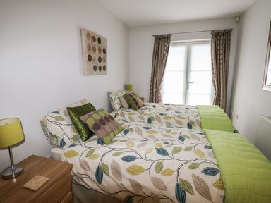 A bedroom with two single beds with leaf patterned bedding and green cushions at 24 Rhodewood House in Saundersfoot