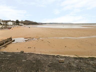 A sandy beach with scattered people and houses along the shoreline at 24 Rhodewood House in Saundersfoot