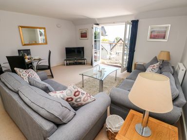 A living room with two grey sofas a glass coffee table a TV and an open balcony door at 24 Rhodewood House in Saundersfoot