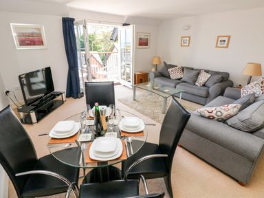A living room with a glass dining table set for four black chairs two grey sofas a glass coffee table television and open balcony doors at 24 Rhodewood House in Saundersfoot