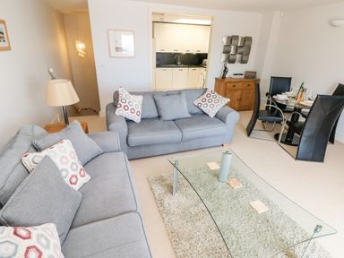 A living room with gray sofas and a glass coffee table near a dining area with black chairs at 24 Rhodewood House in Saundersfoot