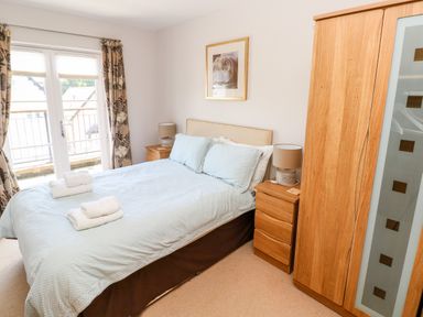 A bedroom with a double bed two bedside tables with lamps a wooden wardrobe and floral curtains at 24 Rhodewood House in Saundersfoot
