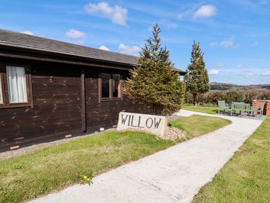 A wooden building with windows a stone sign saying willow a concrete path and outdoor seating at Willow Lodge Lanivet near Bodmin