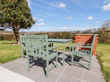 An outdoor patio area with a green table and four green chairs near a brick barbecue and a tree at Willow Lodge in Lanivet near Bodmin