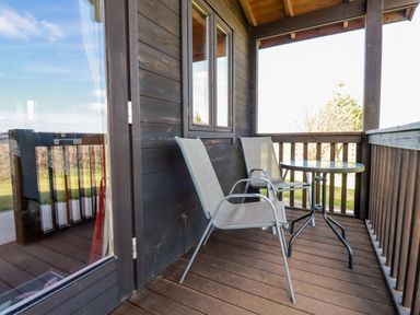 A wooden porch with two metal mesh chairs and a round glass table at Willow Lodge Lanivet near Bodmin