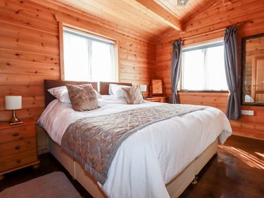 A bedroom with a bed white bedding bedside tables lamps and windows with curtains at Willow Lodge in Lanivet near Bodmin