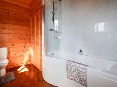 A bathroom with a white bathtub shower and toilet with wood paneled walls and floor at Willow Lodge Lanivet near Bodmin