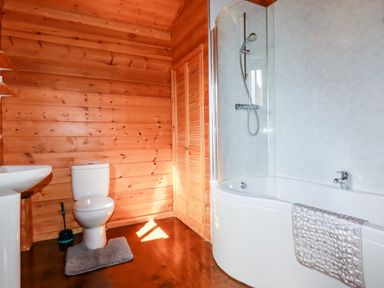 A bathroom with wooden walls a toilet a sink and a bathtub with a shower at Willow Lodge in Lanivet near Bodmin