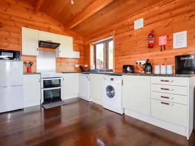 A kitchen with wooden walls and ceiling with white cabinets a refrigerator stove microwave washing machine and countertop appliances at Willow Lodge Lanivet near Bodmin