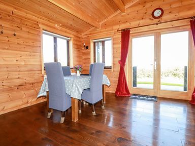 A dining area with a table covered by a star-patterned cloth and four chairs near windows and double glass doors at Willow Lodge Lanivet near Bodmin