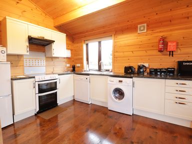 A kitchen with white cabinets black countertop a stove refrigerator dishwasher washing machine and wooden walls at Holly Lodge Lanivet near Bodmin