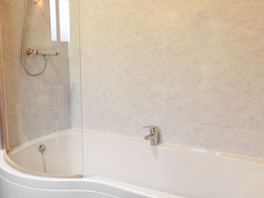 A bathroom with a white bathtub a showerhead and a glass shower screen at Holly Lodge in Lanivet near Bodmin