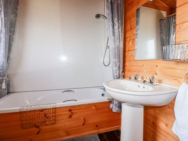 A bathroom with a bathtub shower combination a pedestal sink and wooden paneling on the walls at Hazel Lodge Lanivet near Bodmin
