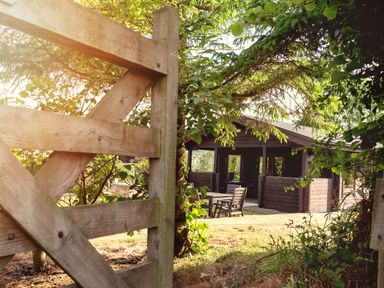 An outdoor wooden gate opening to a garden area with a wooden house and patio furniture at Hazel Lodge in Lanivet near Bodmin
