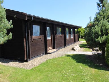 A dark wooden cabin with windows and a door surrounded by grass and trees at Hazel Lodge in Lanivet near Bodmin