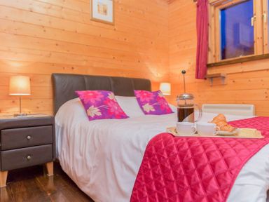 A bedroom with a bed with red pillows and cover with a tray of coffee and croissants at Hazel Lodge in Lanivet near Bodmin
