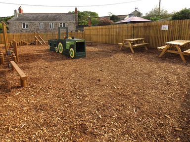 An outdoor play area with a tractor play structure and picnic tables at Hazel Lodge Lanivet near Bodmin