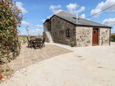 An exterior view of a stone house with a wooden door and window a patio with a table and chairs and outdoor stairs at Sunnywell in Lanivet near Bodmin