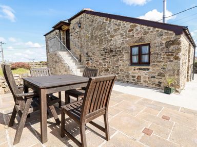 An outdoor patio with a wooden table and four chairs next to a stone building at Sunnywell Lanivet near Bodmin