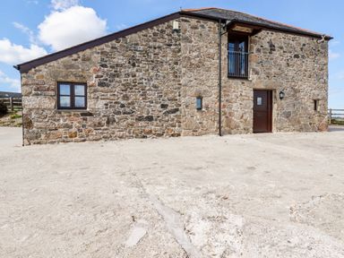 A stone building with a brown door a window and a small balcony at Sunnywell in Lanivet near Bodmin