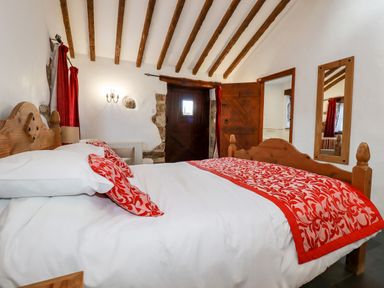 A bedroom with a wooden bed with red and white bedding and red curtains at Sunnywell Lanivet near Bodmin