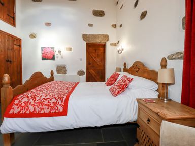 A bedroom with a wooden bed and red patterned bedding near a wooden door at Sunnywell Lanivet near Bodmin