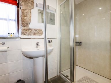 A bathroom with a sink, mirror, shower enclosure, and a window with a red curtain at Sunnywell in Lanivet near Bodmin