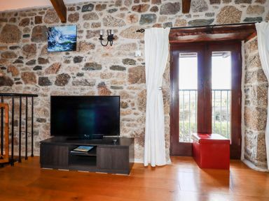 A stone wall living room with a TV on a wooden stand and a red storage box by glass doors at Sunnywell Lanivet near Bodmin