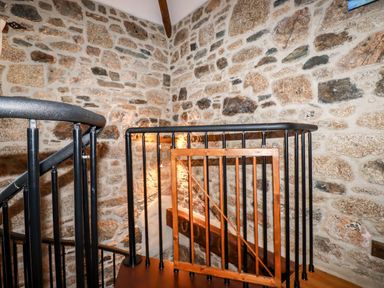 A spiral staircase with black metal railings and wooden gate against a stone wall at Sunnywell in Lanivet near Bodmin