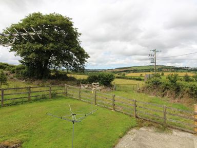 A fenced grassy garden with a rotary clothesline and a large tree overlooking fields and hills at Sunnywell Lanivet near Bodmin