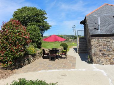 A stone patio with a table and chairs under a red umbrella next to a stone building and garden at Sunnywell Lanivet near Bodmin