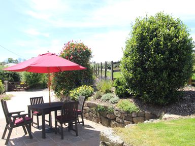 Outdoor patio area with table four chairs and a red umbrella next to shrubbery and a wooden fence at Sunnywell in Lanivet near Bodmin