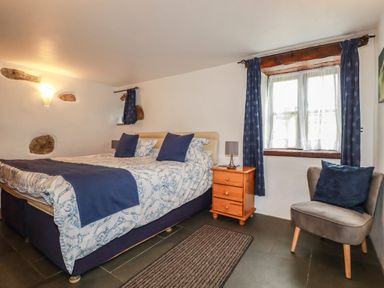A bedroom with a double bed blue and white bedding wooden nightstand and a gray chair by a window at Sunnywell in Lanivet near Bodmin