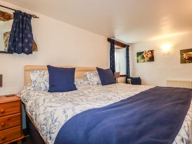A bedroom with a large bed with blue and white bedding two wooden bedside tables and two windows with blue curtains at Sunnywell in Lanivet near Bodmin