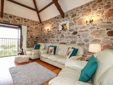 A living room with cream leather sofas green cushions a small wooden side table with a bottle and glasses stone walls and wooden ceiling beams at Sunnywell Lanivet near Bodmin
