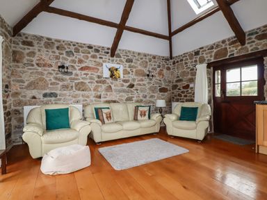 A living room with cream sofas green pillows a small rug wooden floor and stone walls at Sunnywell Lanivet near Bodmin