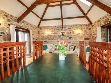 A dining room with wooden chairs a green table and flowers with stone walls and leather sofas at Sunnywell Lanivet near Bodmin