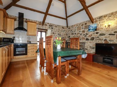 A kitchen dining area with wooden cabinets wooden dining table with chairs and a television on a stand at Sunnywell Lanivet near Bodmin