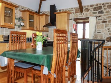 A kitchen with wooden cabinets and a dining table with a green tablecloth and flowers on the table at Sunnywell in Lanivet near Bodmin
