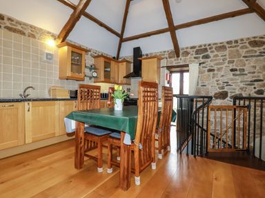 A kitchen with wooden cabinets a table with chairs and a staircase with a gate at Sunnywell Lanivet near Bodmin