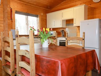 A kitchen with wooden chairs and table with flowers in a vase on the table at Cherry Lodge in Lanivet near Bodmin