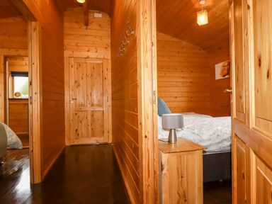 A wooden hallway with multiple wooden doors and a bedroom with a bed and bedside table at Cherry Lodge in Lanivet near Bodmin