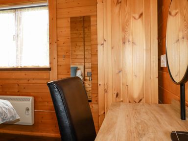 A wooden room with a black chair a wooden desk a window with white curtains and a wall mirror at Cherry Lodge Lanivet near Bodmin